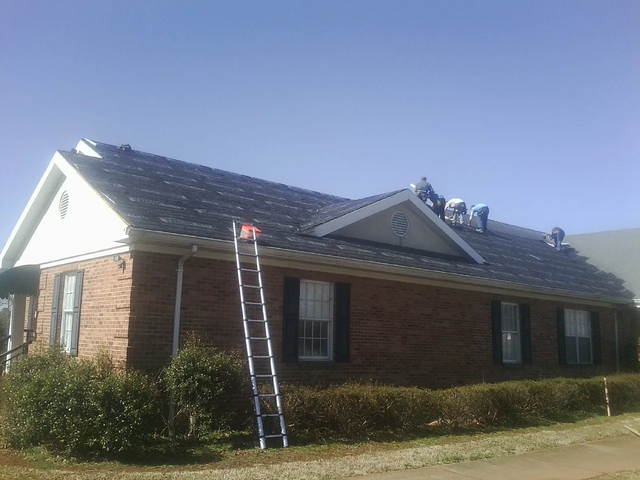 Crew tearing shingles off a brick ranch roof with a ladder set — Metal Roof Repair work by our crew in Whately