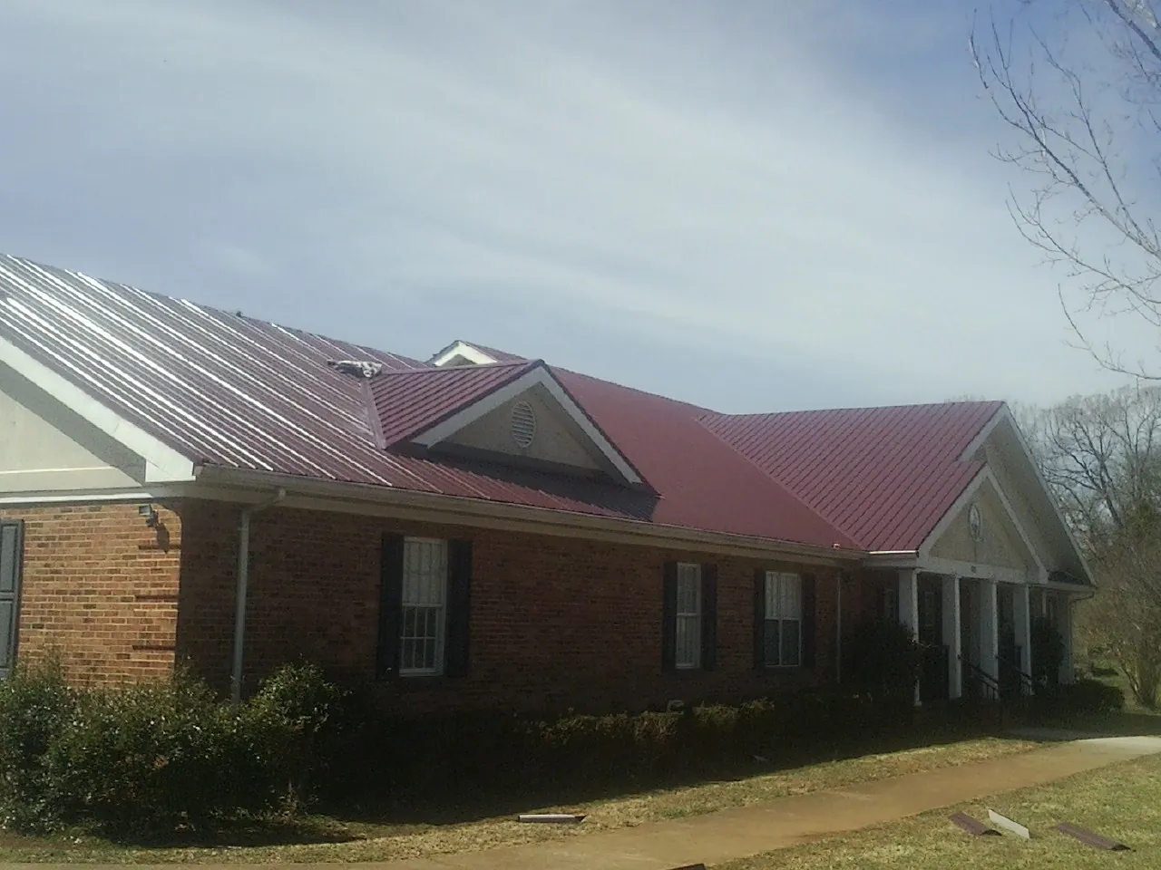 Red metal roof with gabled entries on a long brick building, from a Hail Damage Roof Repair job in Whately