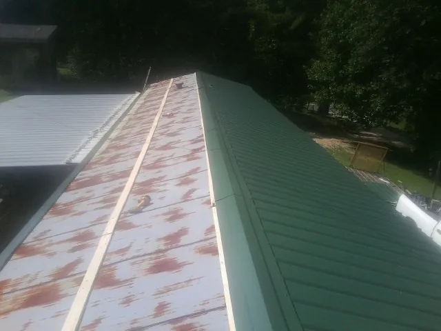 Old rusted panels beside newly installed green metal roofing — Wind Damage Roof Repair by Roofing Brothers in Whately