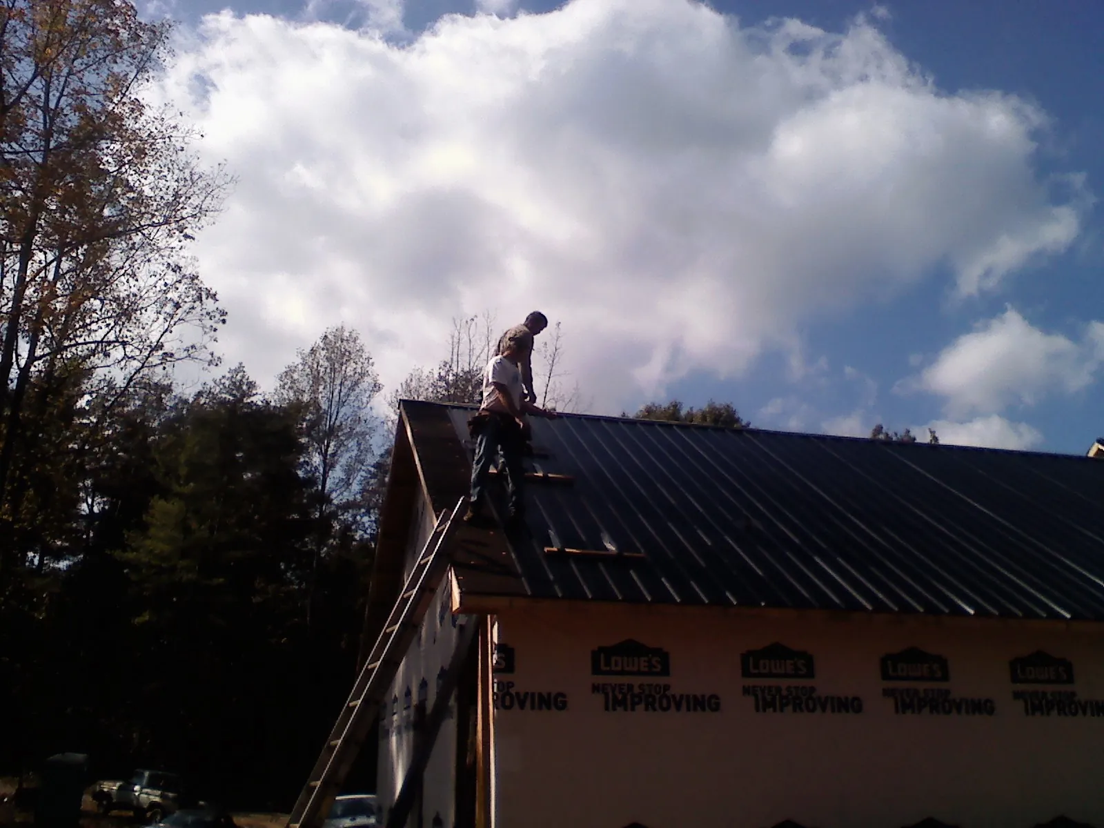 Roofer fastening dark metal panels high against a cloudy sky, from a Roof Inspection job in Whately