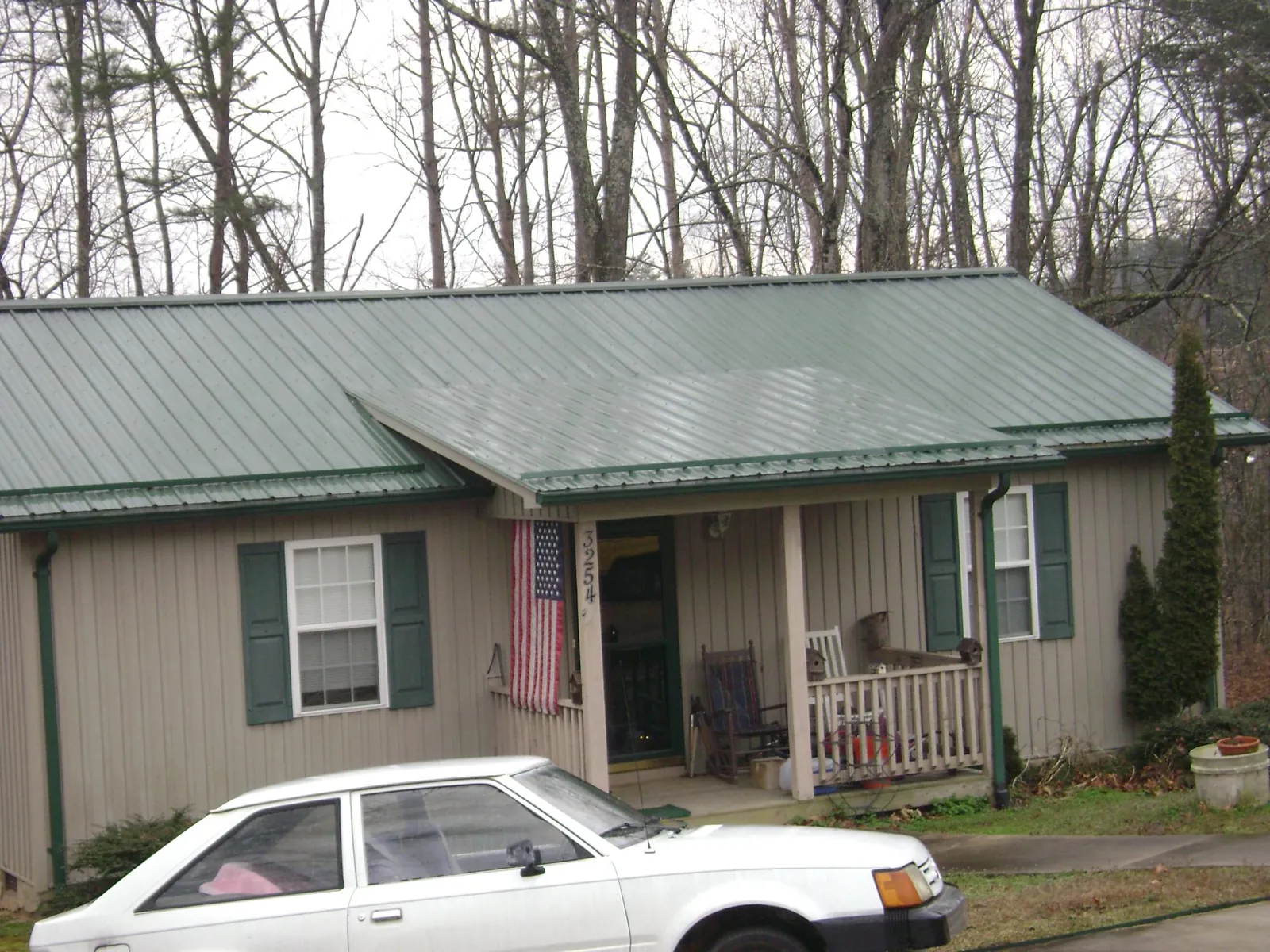 Green metal roof and front porch on a tan sided cottage in Whately